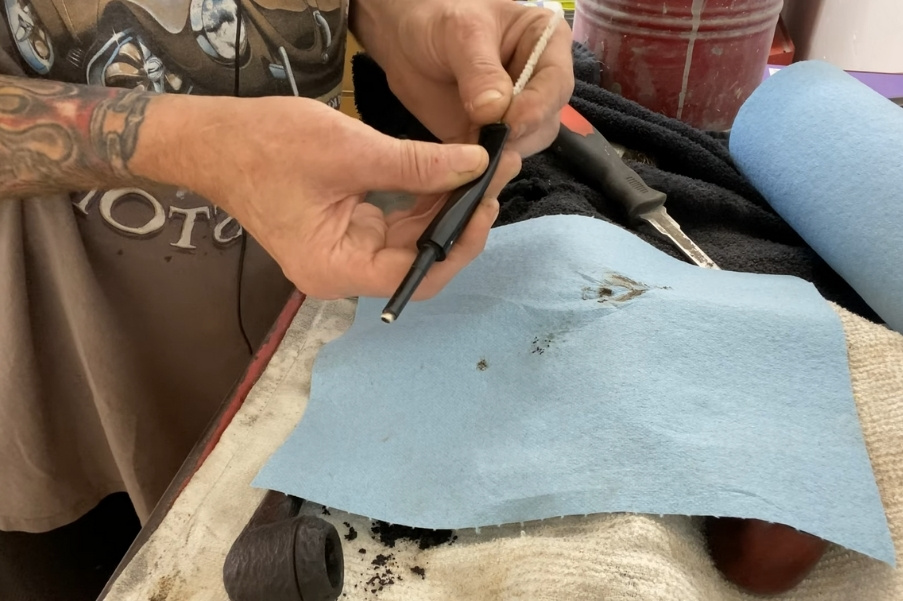 Persona che pulisce il bocchino della pipa con uno scovolino su un banco da lavoro.